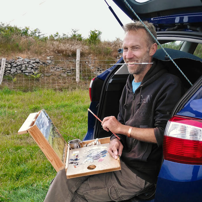 A photograph of Welsh artist Chris Chalk painting outdoors in the Welsh landscape using a pochade box and painting from his car.