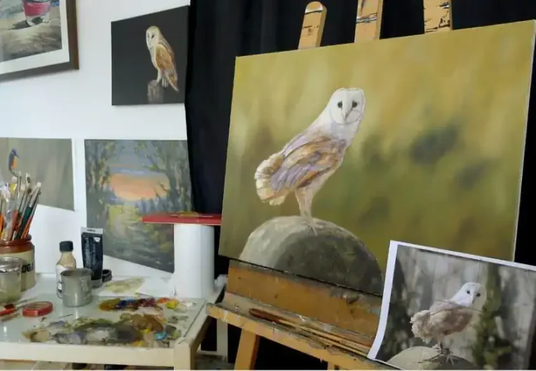 A painting of a barn owl on a artist's easel in a studio full of beautiful paintings.